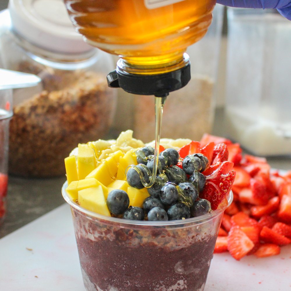 Honey drizzled over a fresh açaí bowl with mango, blueberry and strawberry